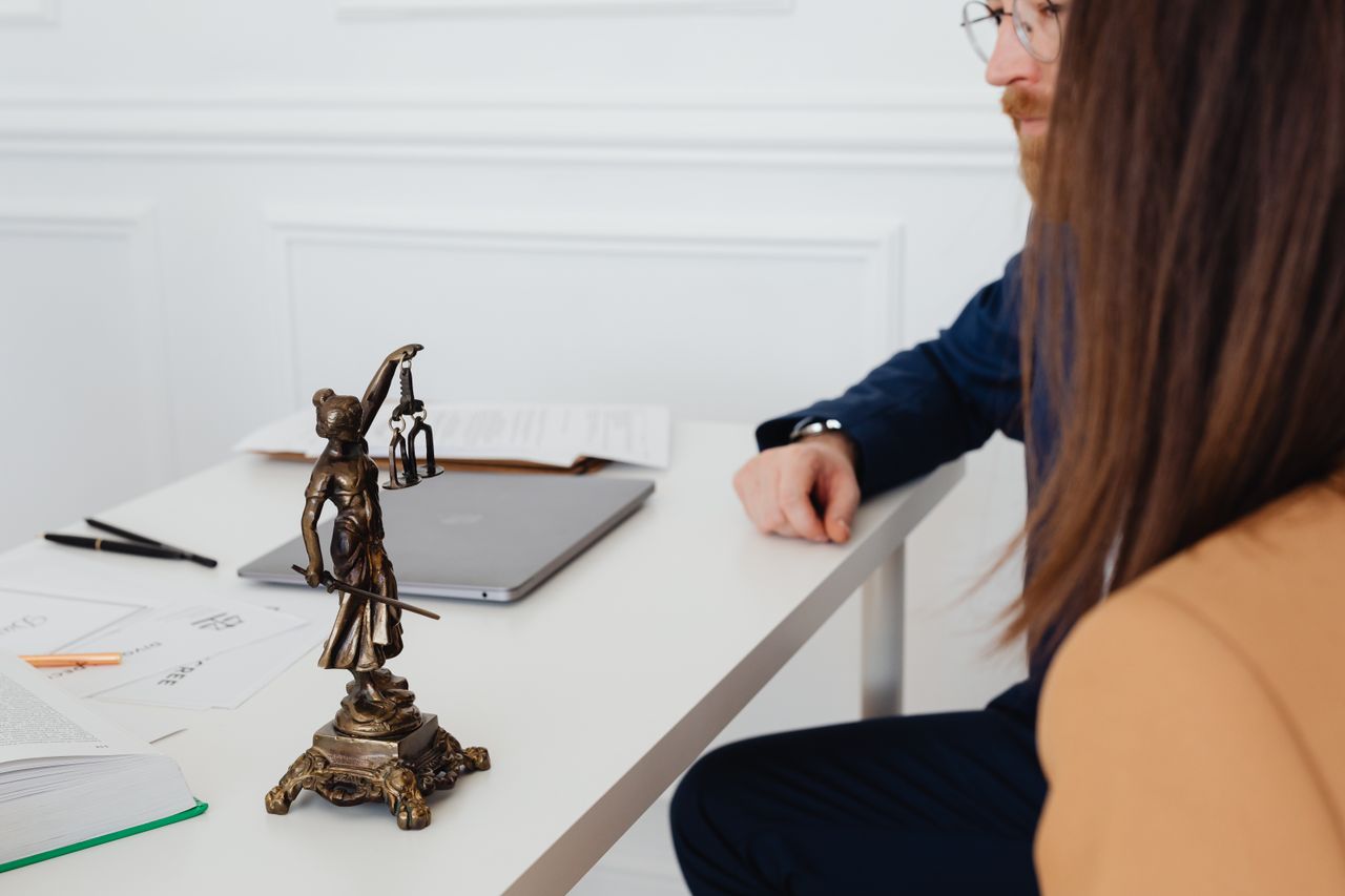heros-img Professional setting with lawyers and Lady Justice statue discussing legal documents.